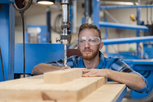 Porträt eines Zimmermanns mit Schutzbrille beim Bohren von Holzbrettern - DIGF14232