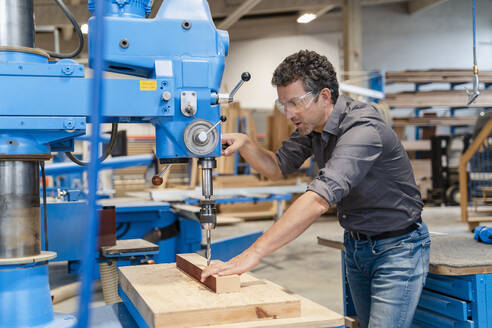 Schreiner mit Schutzbrille beim Bohren von Holzbrettern in einer Produktionshalle - DIGF14233