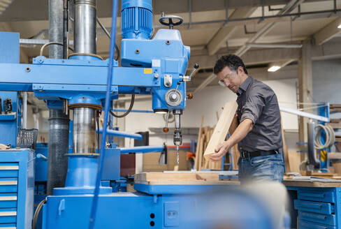 Schreiner mit Schutzbrille beim Bohren von Holzbrettern in einer Produktionshalle - DIGF14234