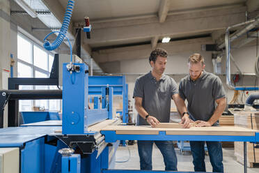 Two carpenters talking while examining wood in production hall - DIGF14249