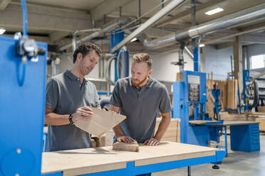 Two carpenters talking while examining wood in production hall - DIGF14250