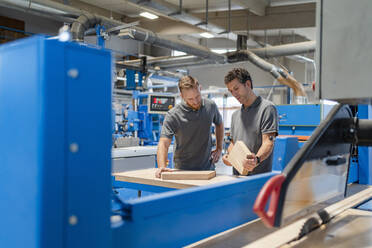 Two carpenters talking while examining wood in production hall - DIGF14252