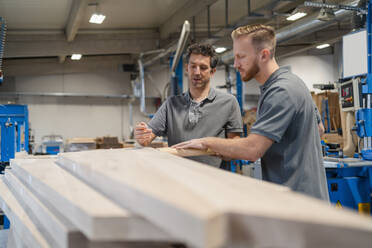 Zwei Zimmerleute prüfen Holzbretter in der Produktionshalle - DIGF14265