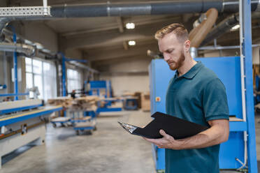 Porträt eines Schreiners in einer Produktionshalle mit einem Klemmbrett in der Hand - DIGF14271