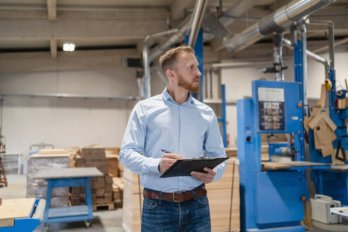 Porträt eines Schreiners in einer Produktionshalle mit einem Klemmbrett in der Hand - DIGF14289