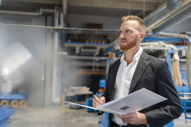 Portrait of well-dressed carpenter standing in production hall with ring binder in hands - DIGF14297