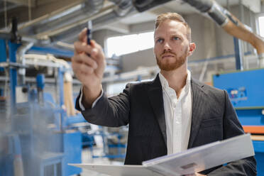 Porträt eines gut gekleideten Schreiners in einer Produktionshalle mit einem Ringbuch in der Hand - DIGF14298