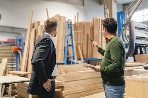 Zwei Zimmerleute im Gespräch vor gestapelten Holzbrettern in einer Produktionshalle - DIGF14301
