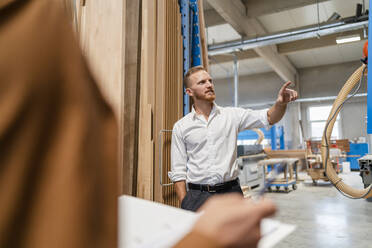 Two carpenters talking while examining planks in production hall - DIGF14311