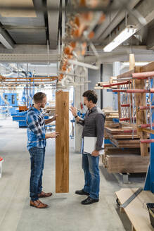 Zwei Zimmerleute inspizieren Holzbretter in der Produktionshalle - DIGF14318