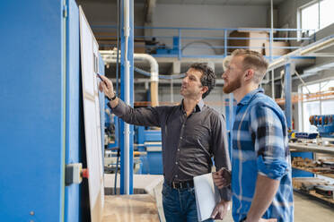 Two carpenters talking over documents in production hall - DIGF14322