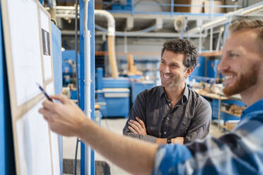 Two carpenters talking over documents in production hall - DIGF14324