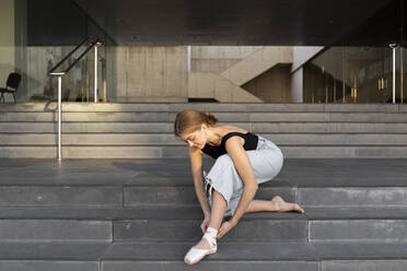 Ballerina beim Binden des Ballettschuhs auf der Treppe - JPTF00634
