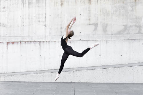 Ballerina im schwarzen Trikot springt vor einer Betonwand - JPTF00642