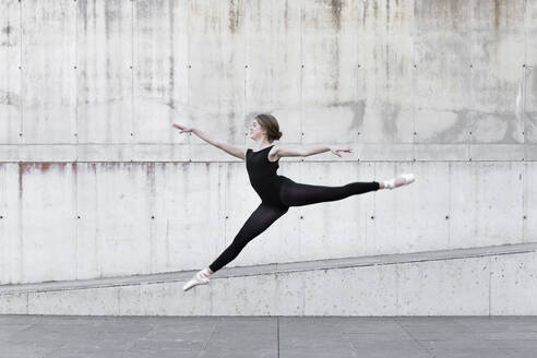 Ballerina im schwarzen Trikot springt vor einer Betonwand - JPTF00643