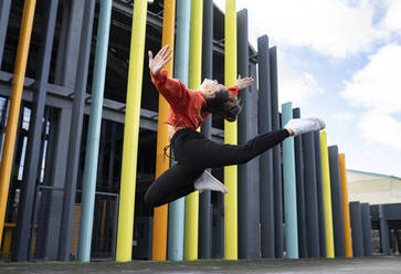 Portrait of beautiful brunette jumping in front of colorful building - JCCMF00764