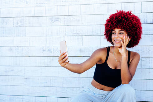 Frau mit rotem Afro-Haar macht ein Selfie mit Handy. - CAVF91583