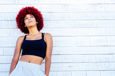 Frau mit rotem Afro-Haar, die an einer weißen Wand steht. - CAVF91585
