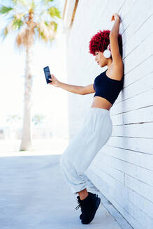 Woman with red afro hair listening music with headphones. - CAVF91586