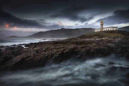 A beautiful lighthouse on a hill with its light on at sunset - CAVF91615