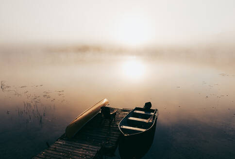 Leerer Steg mit festgemachten Booten an einem nebligen Morgen auf einem ruhigen See. - CAVF91652