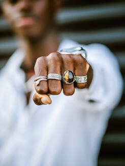Blurred anonymous African American stylish male showing fist with various trendy silver rings - ADSF19723