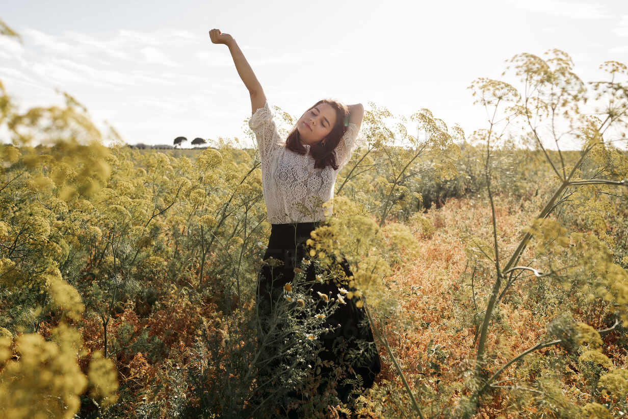 Young attractive female relaxing standing in meadow with arms raise in ...