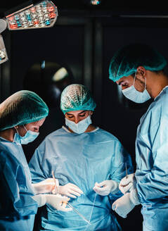 Eine Gruppe konzentrierter professioneller Chirurgen mit chirurgischen Instrumenten und Fäden, die die Operation eines Patienten im Operationssaal beenden - ADSF19740