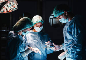 Eine Gruppe konzentrierter professioneller Chirurgen mit chirurgischen Instrumenten und Fäden, die die Operation eines Patienten im Operationssaal beenden - ADSF19741