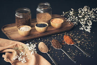 Top view of assorted grains in jars and aromatic spices in spoons arranged on wooden tray on black table - ADSF19757
