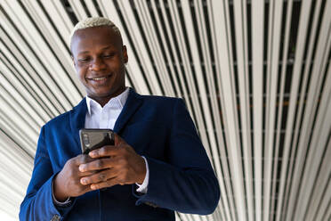 From below of elegant African American male entrepreneur browsing smartphone on street and checking business issues - ADSF19790