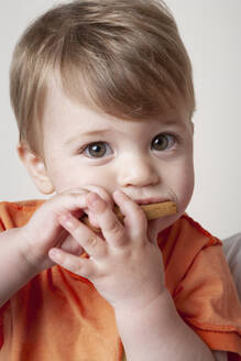 Baby boy in orange t-shirt eating biscuit - ISPF00006