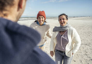 Group of friends talking and laughing at sandy beach - UUF22498
