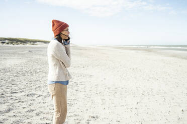 Porträt einer Frau mit Strickmütze, die am Strand mit ihrem Smartphone telefoniert - UUF22505