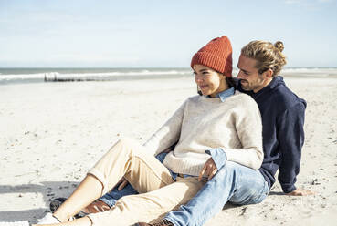 Junges Paar sitzt zusammen am Strand - UUF22519