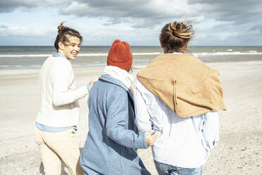 Group of friends walking together along sandy coastal beach - UUF22538