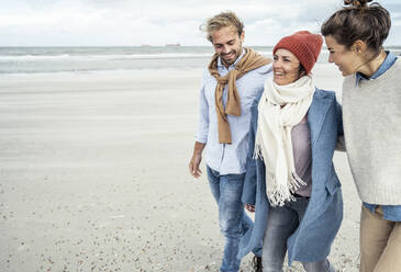 Group of friends walking together along sandy coastal beach - UUF22539