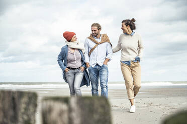 Group of friends walking together along sandy coastal beach - UUF22544