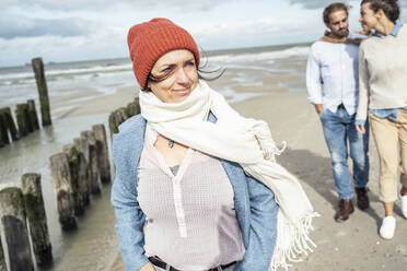 Porträt einer jungen Frau mit Schal und Strickmütze am Strand stehend - UUF22545