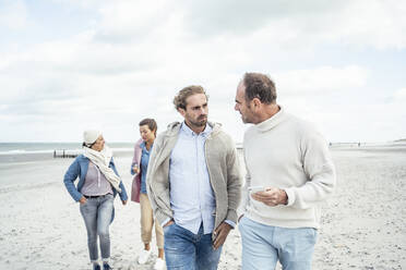 Two men walking and talking side by side along sandy beach - UUF22548