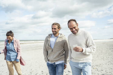 Two men walking and talking side by side along sandy beach - UUF22549