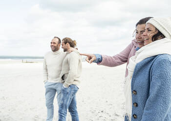 Group of adult friends standing and talking on coastal beach - UUF22552