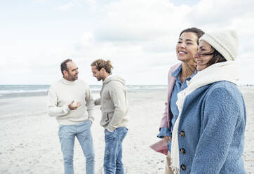 Group of adult friends standing and talking on coastal beach - UUF22553