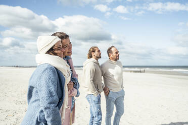 Group of adult friends standing and talking on coastal beach - UUF22554