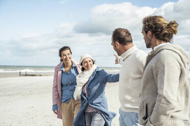 Group of adult friends greeting on coastal beach - UUF22555