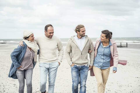 Group of adult friends walking side by side along sandy beach stock photo