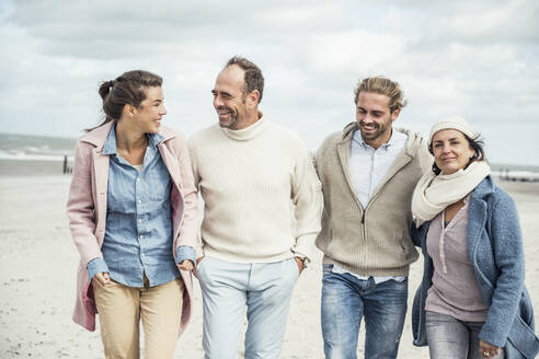 Gruppe erwachsener Freunde, die Seite an Seite am Sandstrand spazieren gehen - UUF22576