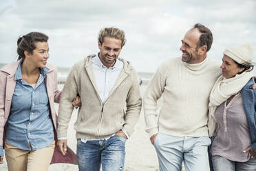 Group of adult friends walking side by side along sandy beach - UUF22577