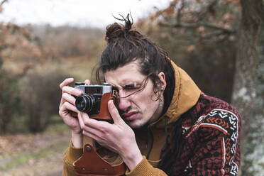 Young man photographing Autumn landscape with vintage camera - JAQF00182