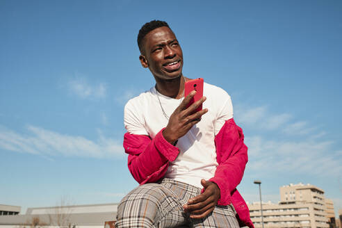 Young man in red jacket looking at smart phone outdoors - AODF00221